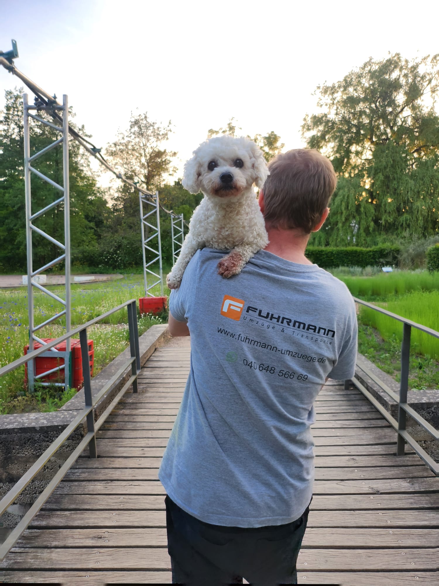 Fuhrmann-Mitarbeiter im grauen Firmen-T-Shirt trägt einen kleinen weißen Hund auf der Schulter